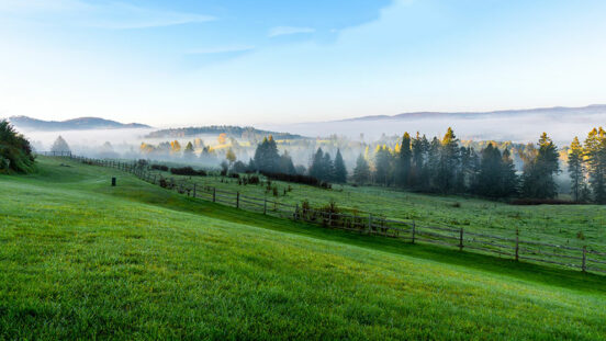 Image of grass fields and mountains in the background with fog rising