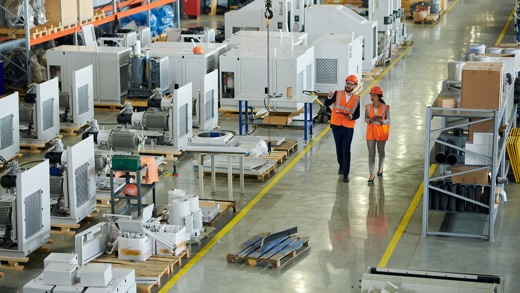Two people in safety vests walking along a manufacturing floor
