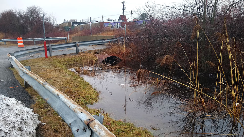 flooded culvert next to a road and guardrail
