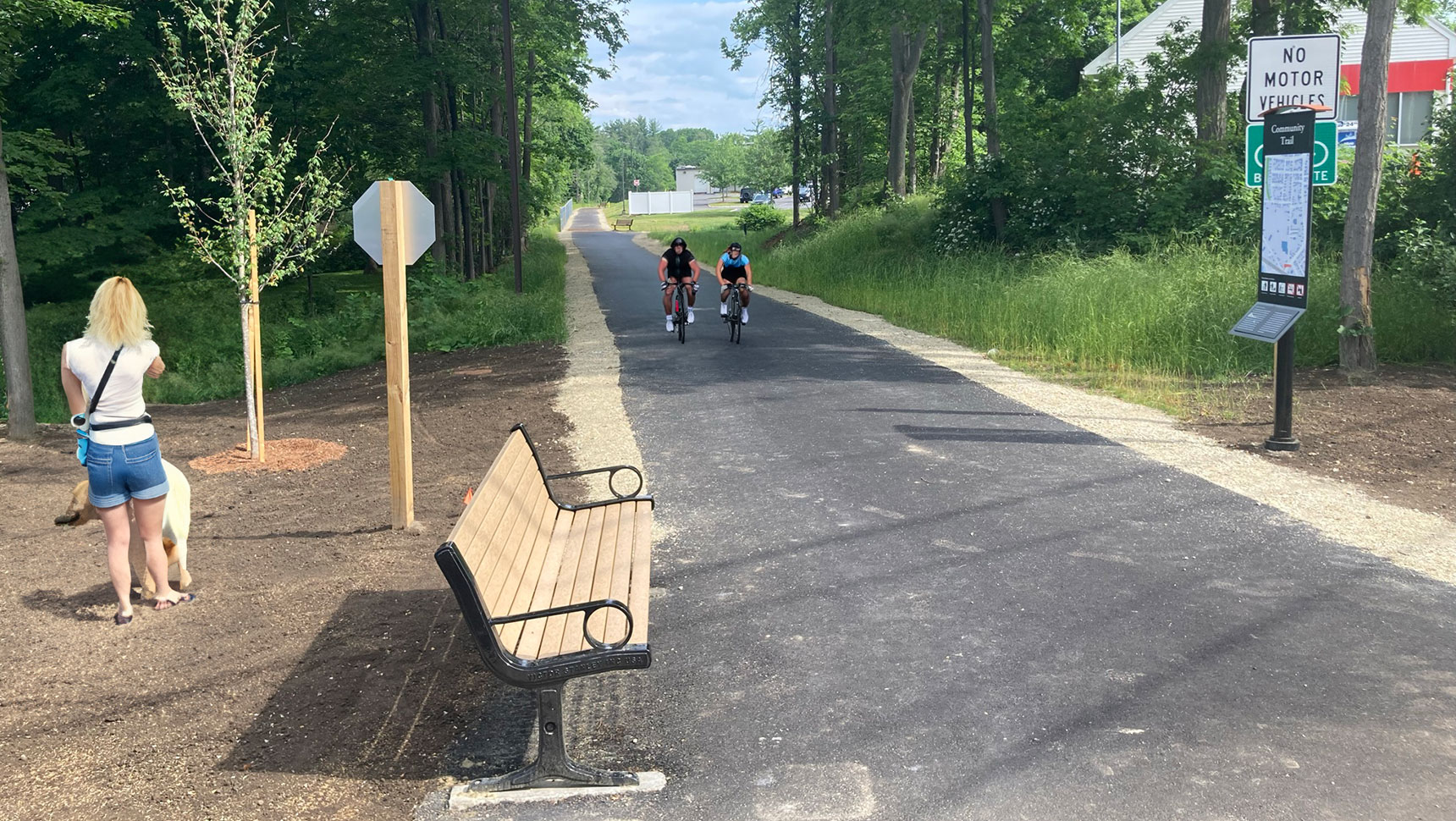 Woman with a dog on the side of the trail and two bikers on the trail