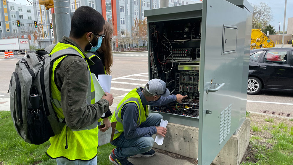 Three people with safety vests inspect traffic control equipment