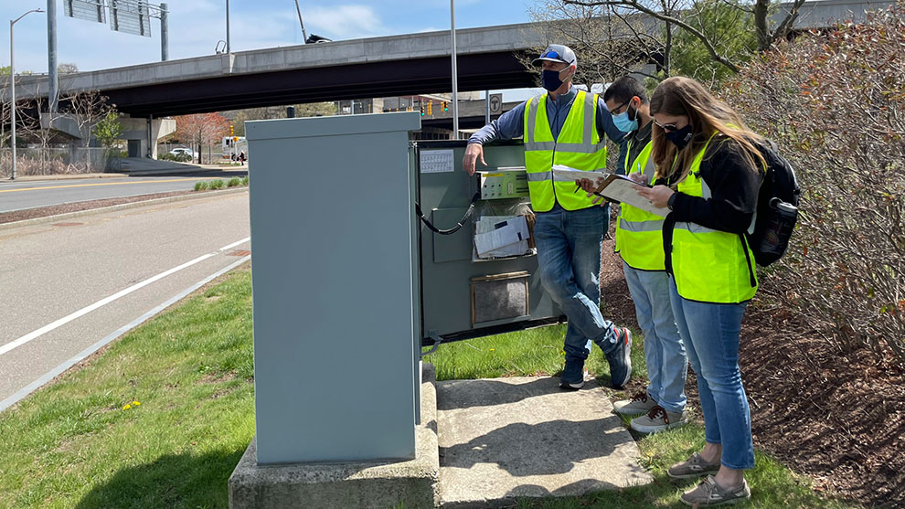 Three people with safety vests inspecting traffic control equipment