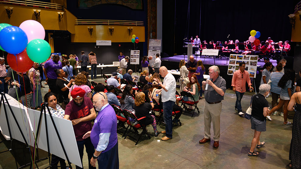 wall street community event in a room decorated with balloons and people sitting in seats, people walking, and people standing around talking